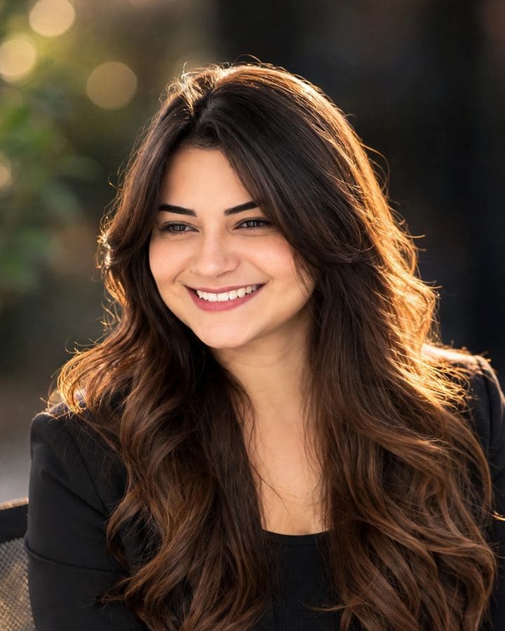 Giovanna Oliveira sorrindo, de blazer preto, com luz dourada ao fundo